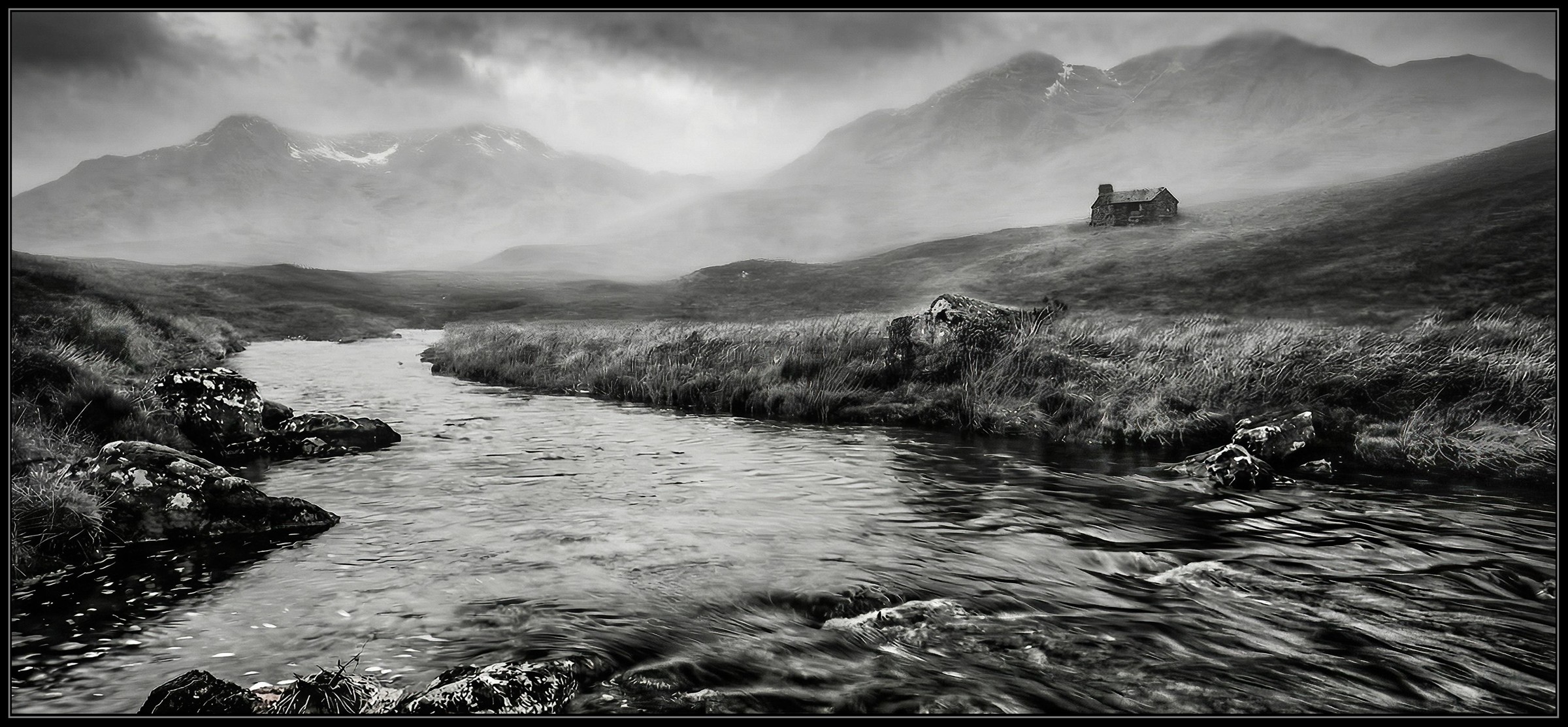 Black-and-white photograph of a stream winding through misty mountains, with a small cottage on the hillside